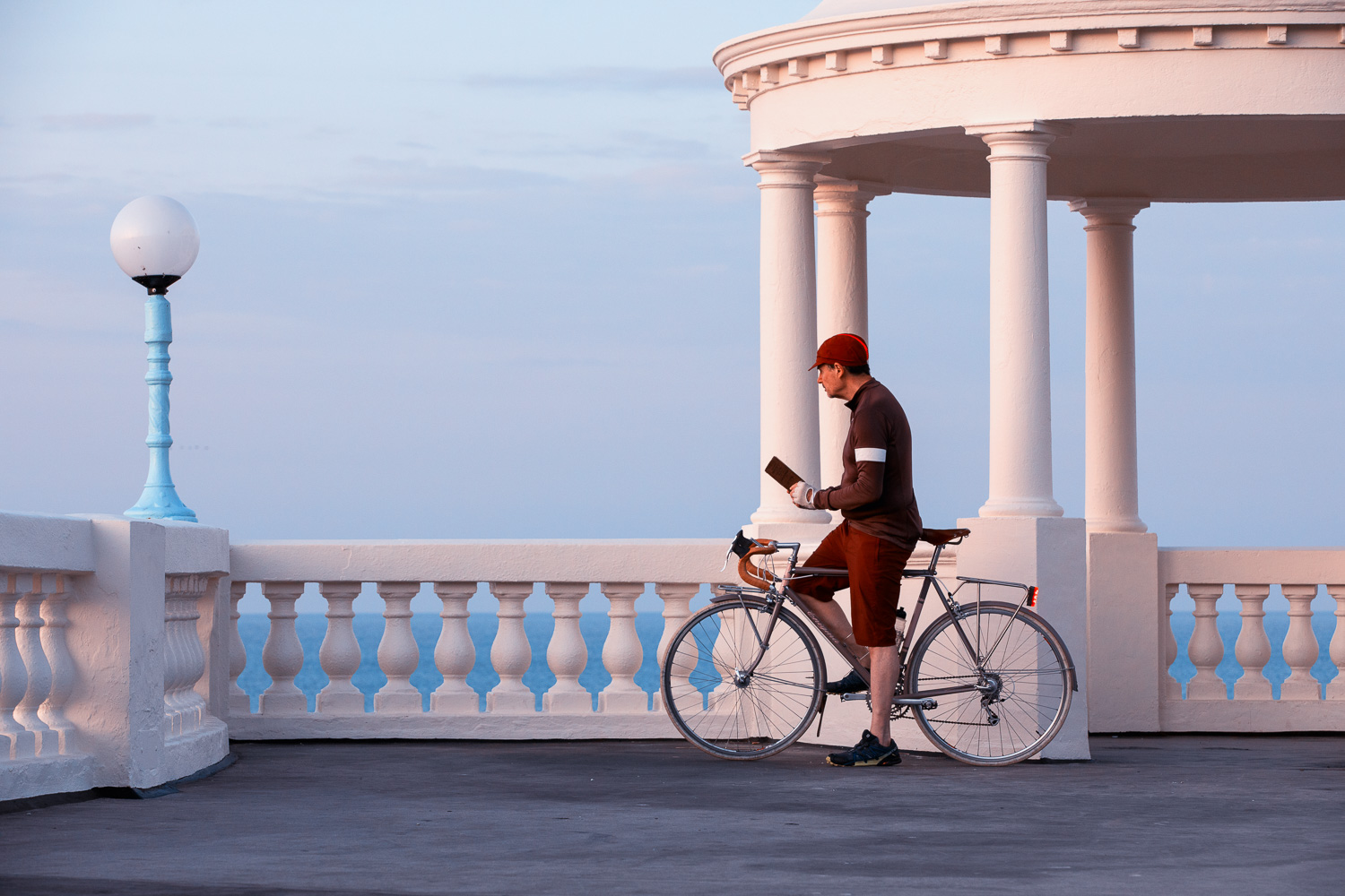 A posed cyclist studies a map in from of Tuscan columns and a classical balustrade at the King George V Colonnade in Bexhill-on-Sea