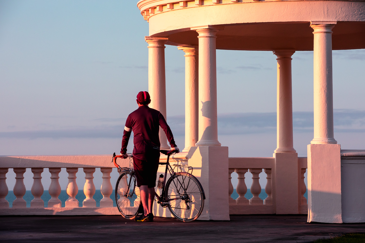 Cyclist poses in the neo classic setting of the King George V Colonnade on the seafront at Bexhill-on-Sea, East Sussex
