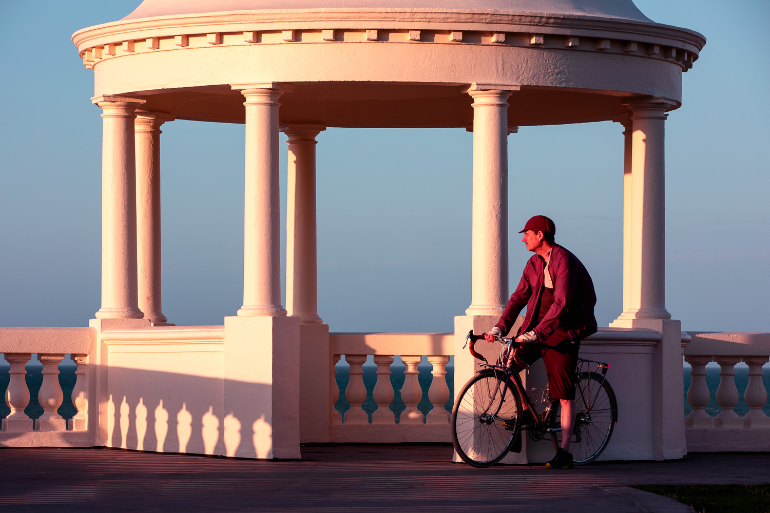 Cyclist and photographer Roff Smith poses with his classic touring bicycle by the Tuscan pillars and neoclassic dome of the King George V Colonnade on the seafront at Bexhill on Sea at dawn on a fine summer morning