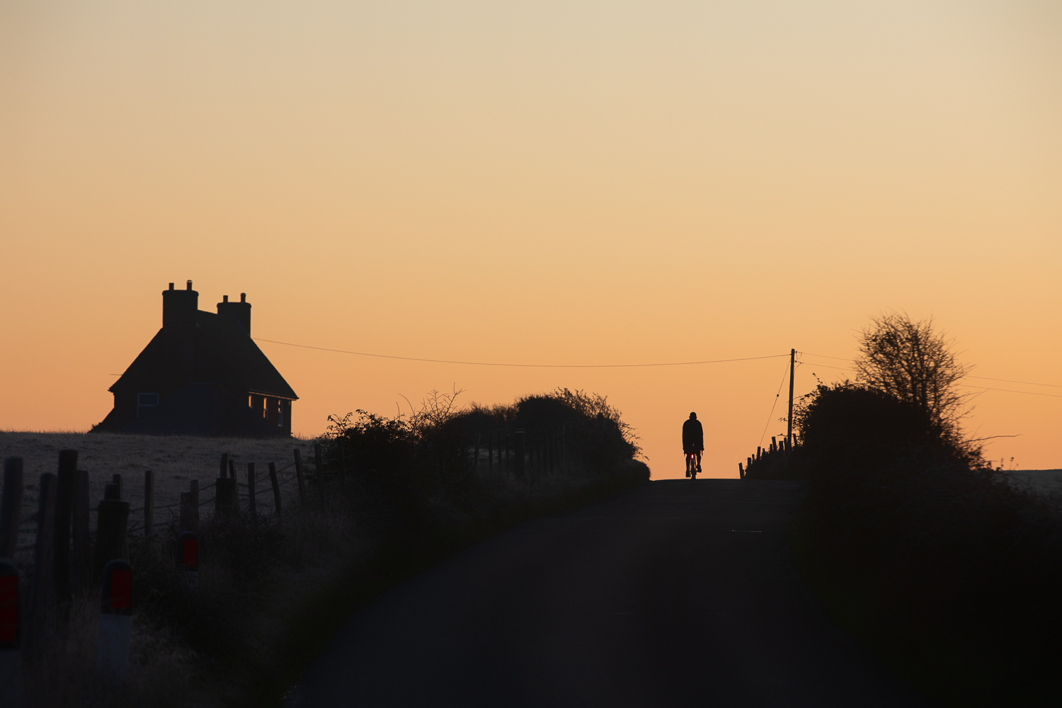Early morning cyclist backlit by coppery sunrise, near Pevensey, East Sussex