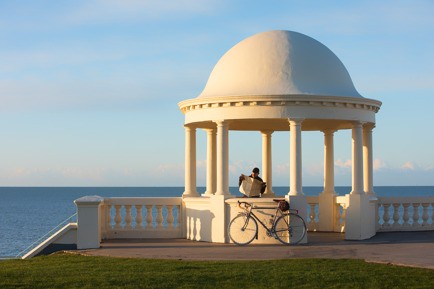 Mad with bicycle reading map by neo-classical dome by the seaside in bright