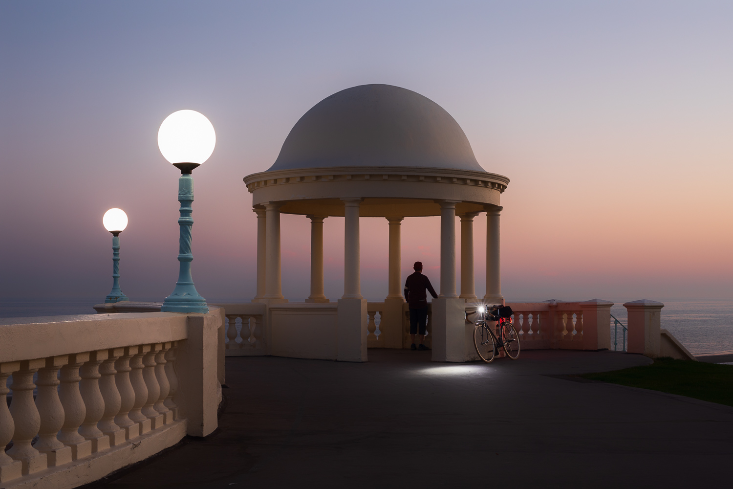 Man with bicycle looking out to see at twilight by classical colonnade