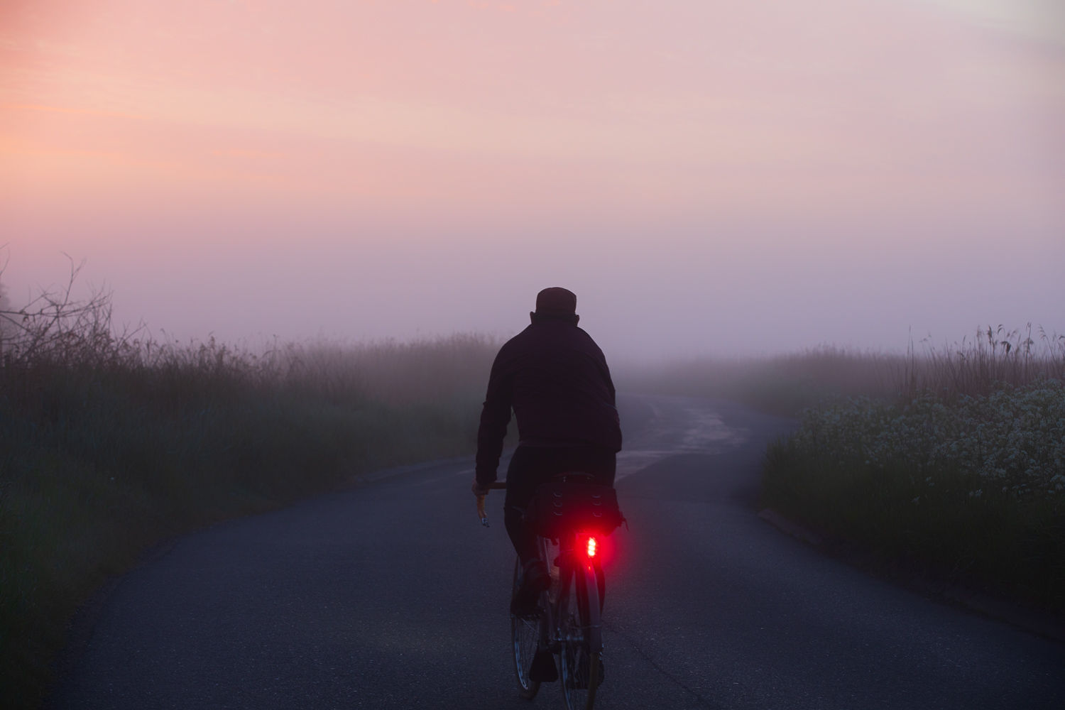 Cyclist with red taillight riding into violet mist at dawn