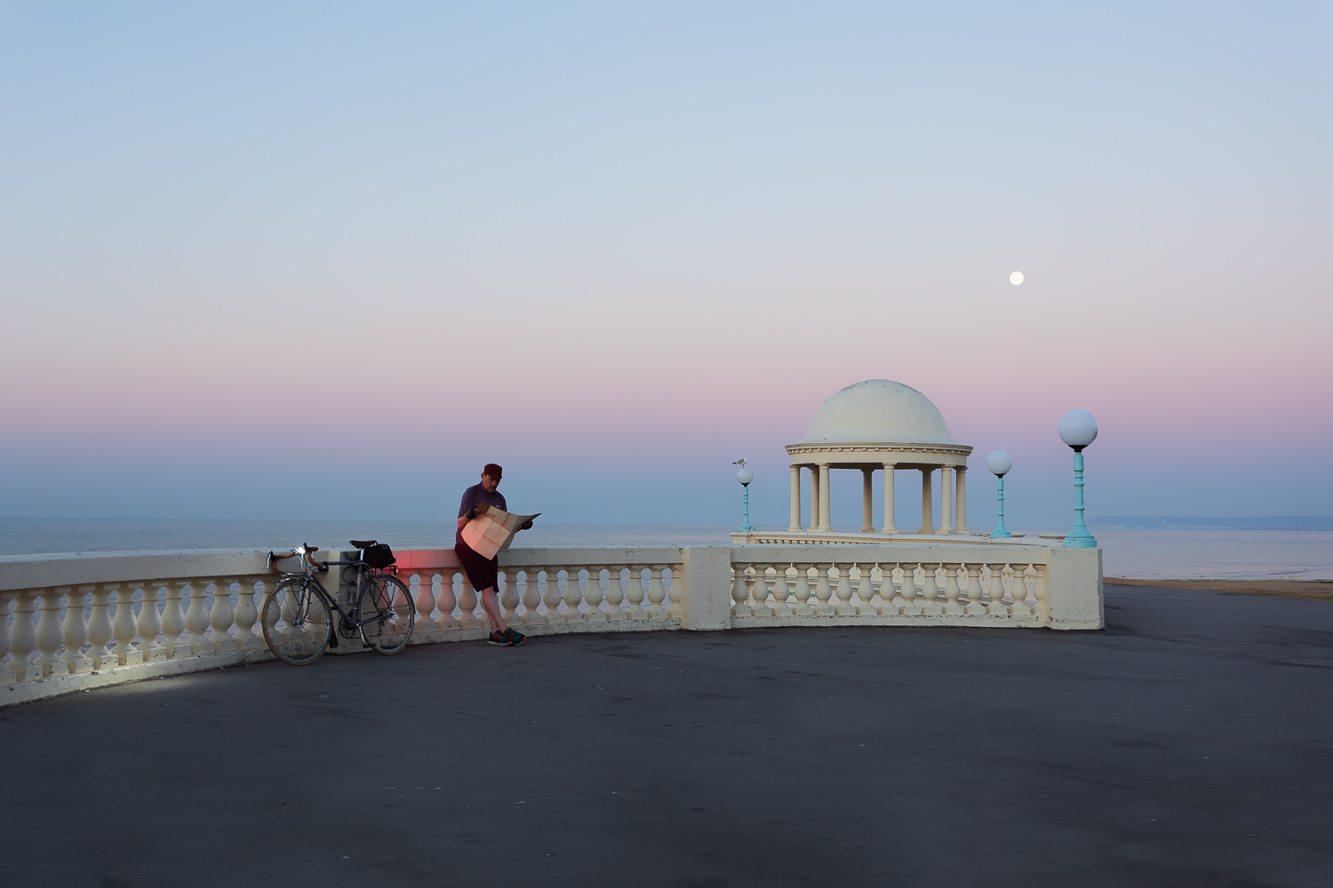 Cyclist reading map beside old seaside monument at dawn